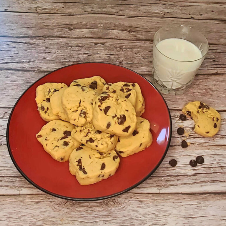 A red plate with peanut butter shortbread cookies on it, next to a glass of milk and a partly eaten cookie with chocolate chips.