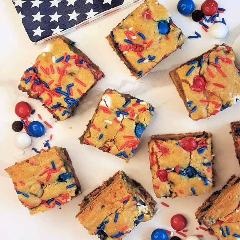 Red, white and blue cookie bars on parchment paper near a flag napkin and loose MM candies.