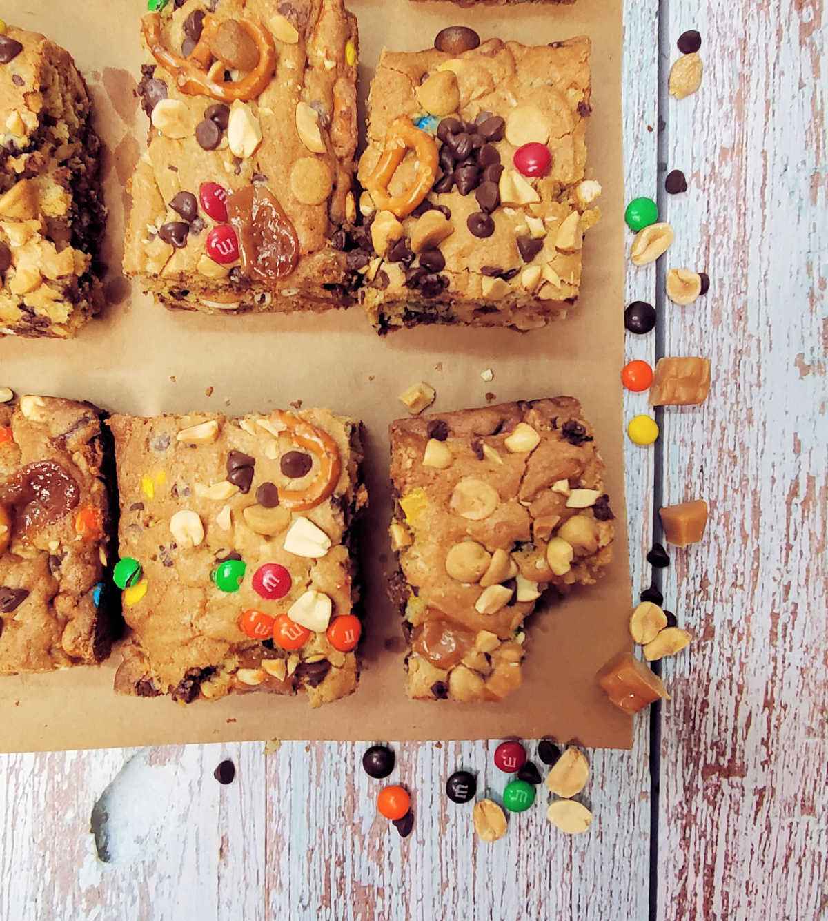 Kitchen sink dessert bars cut into slices. One has a bite out of it. Bars are sitting next to M & Ms and chocolate chips.