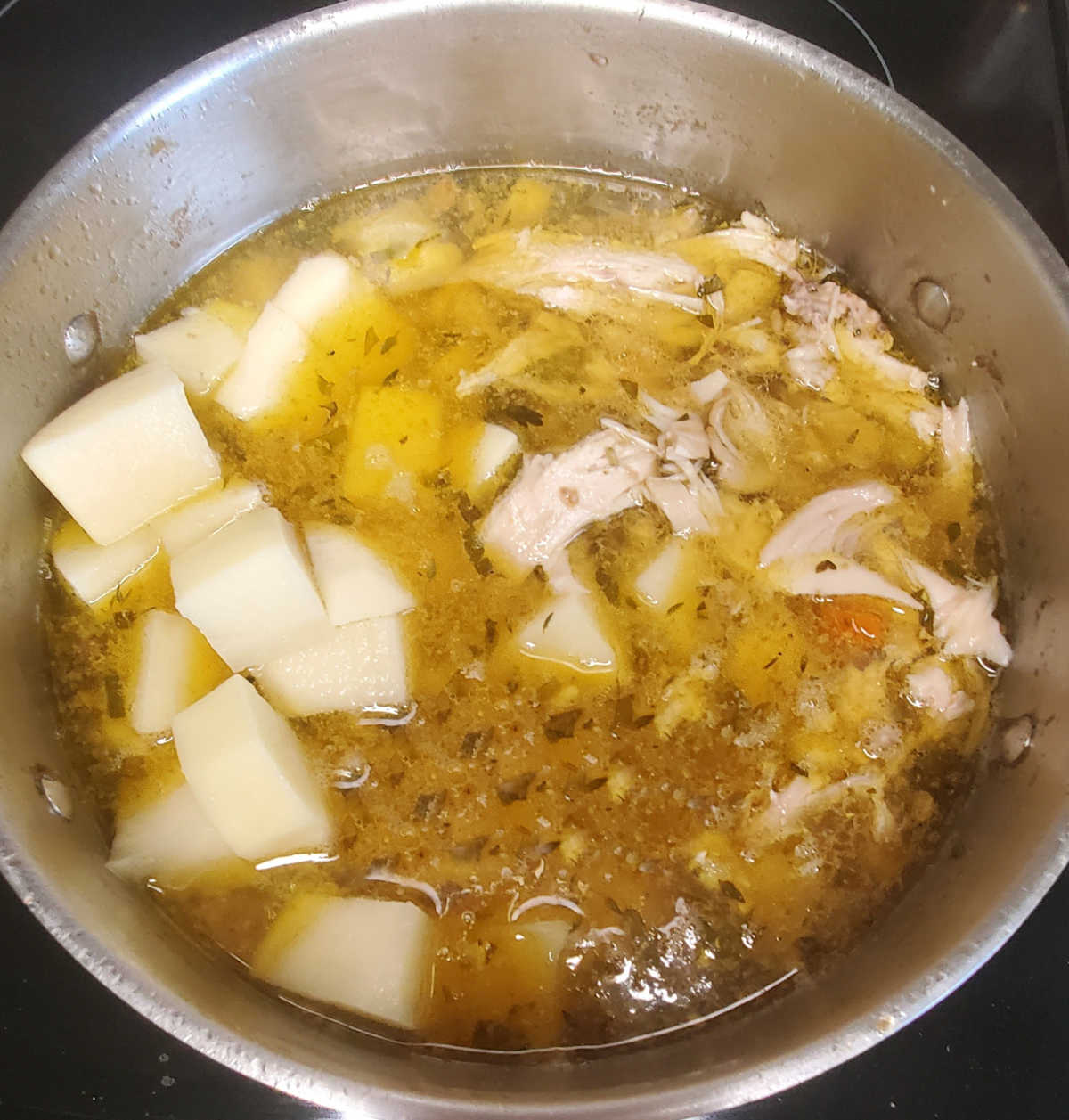 Add the potatoes and shredded chicken to the pot. A large pot with broth and potato and chicken pieces sitting in the broth.