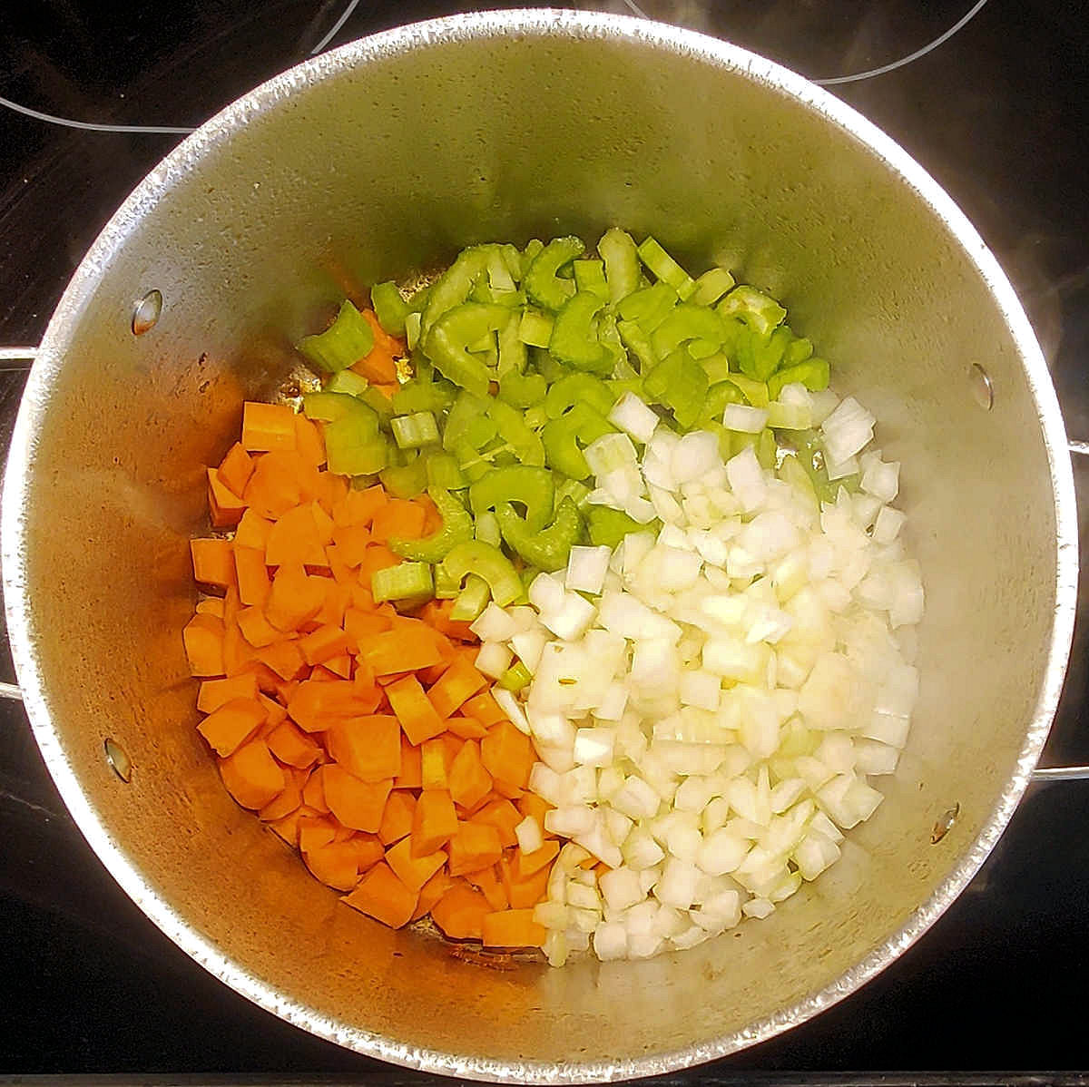 Cook the vegetables A large pot with diced carrots, celery and onion in the bottom of it ready to cook a chicken and dumplings recipe.