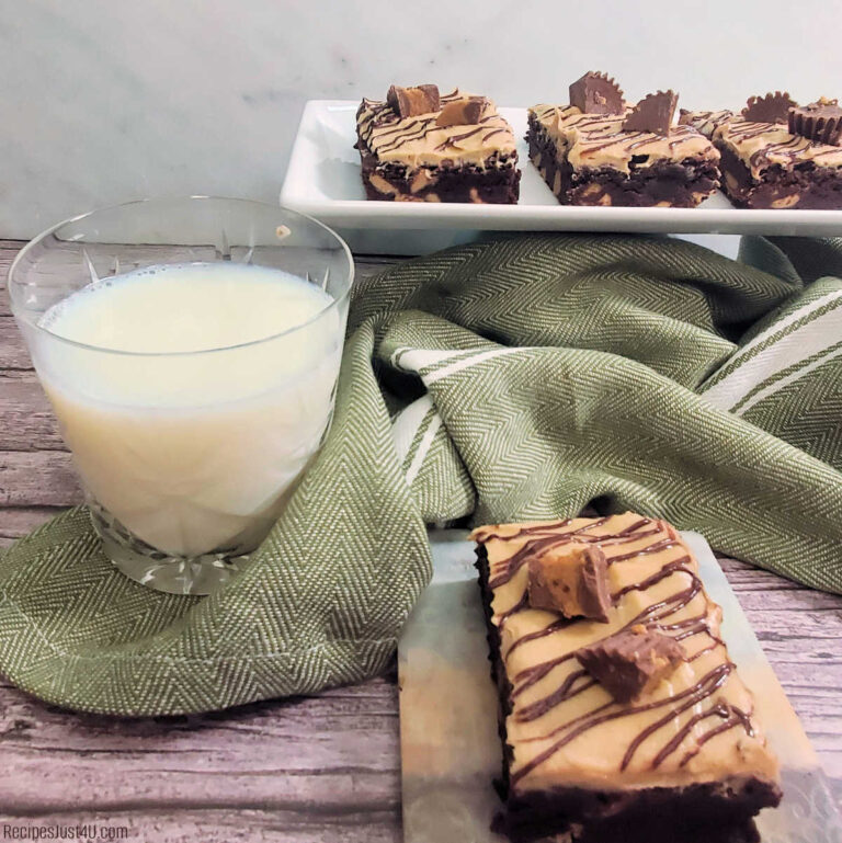 A glass of milk, green towel, brownie and tray of brownies with peanut butter icing on a counter top.