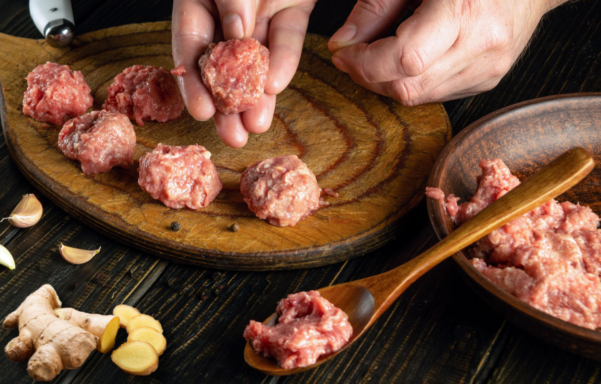 Hands forming Asian meatballs.
