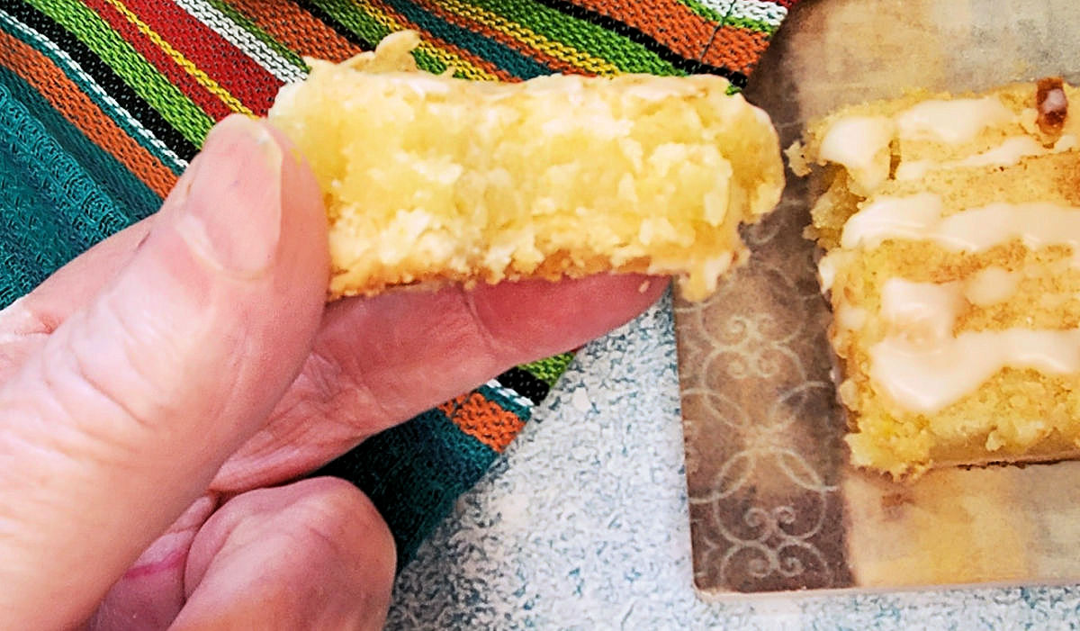 A hand holding a lemon bar with a bite out of it.