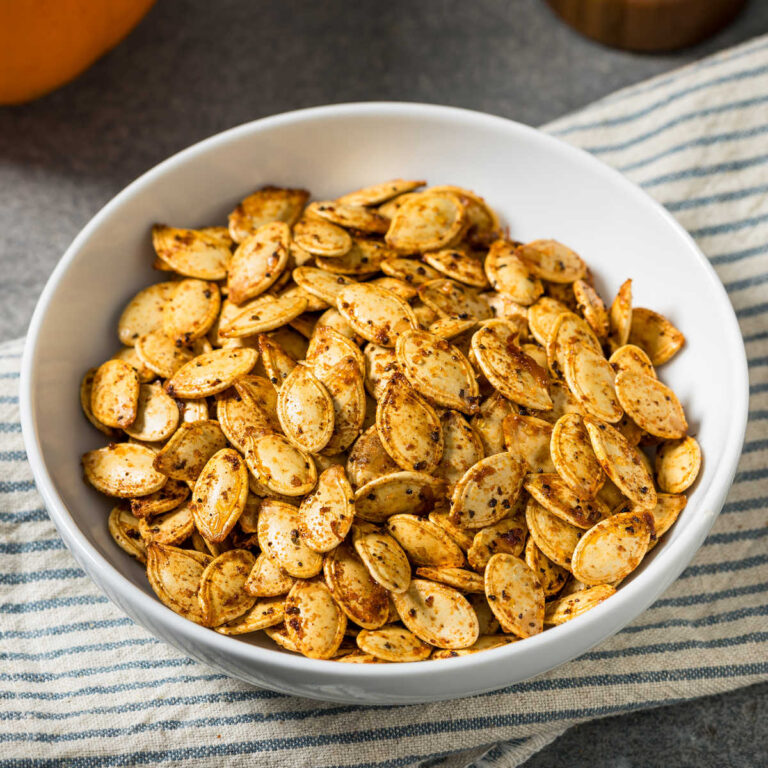 Pumpkin pie spiced pumpkin seeds in a bowl on a gray striped towel.