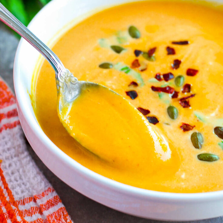 Pumpkin soup in a white bowl with a spoon.
