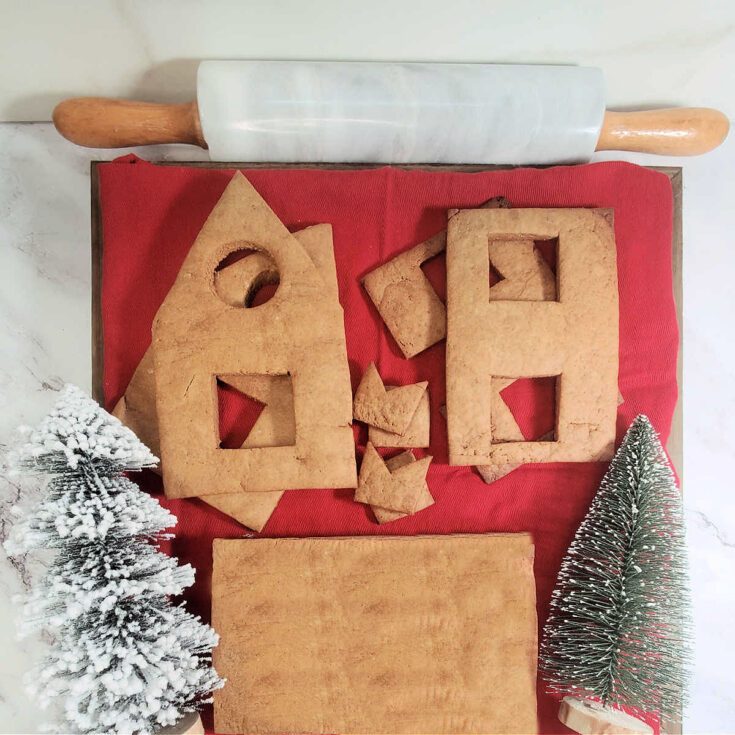 Homemade gingerbread dough pieces stack on a red napkin next to a marble rolling pin and two faux Christmas trees.