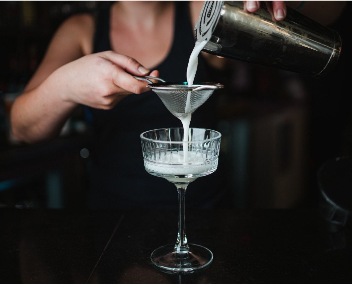 A bartender displaying a cocktail trick, which is double straining a cocktail into a coupe glass.