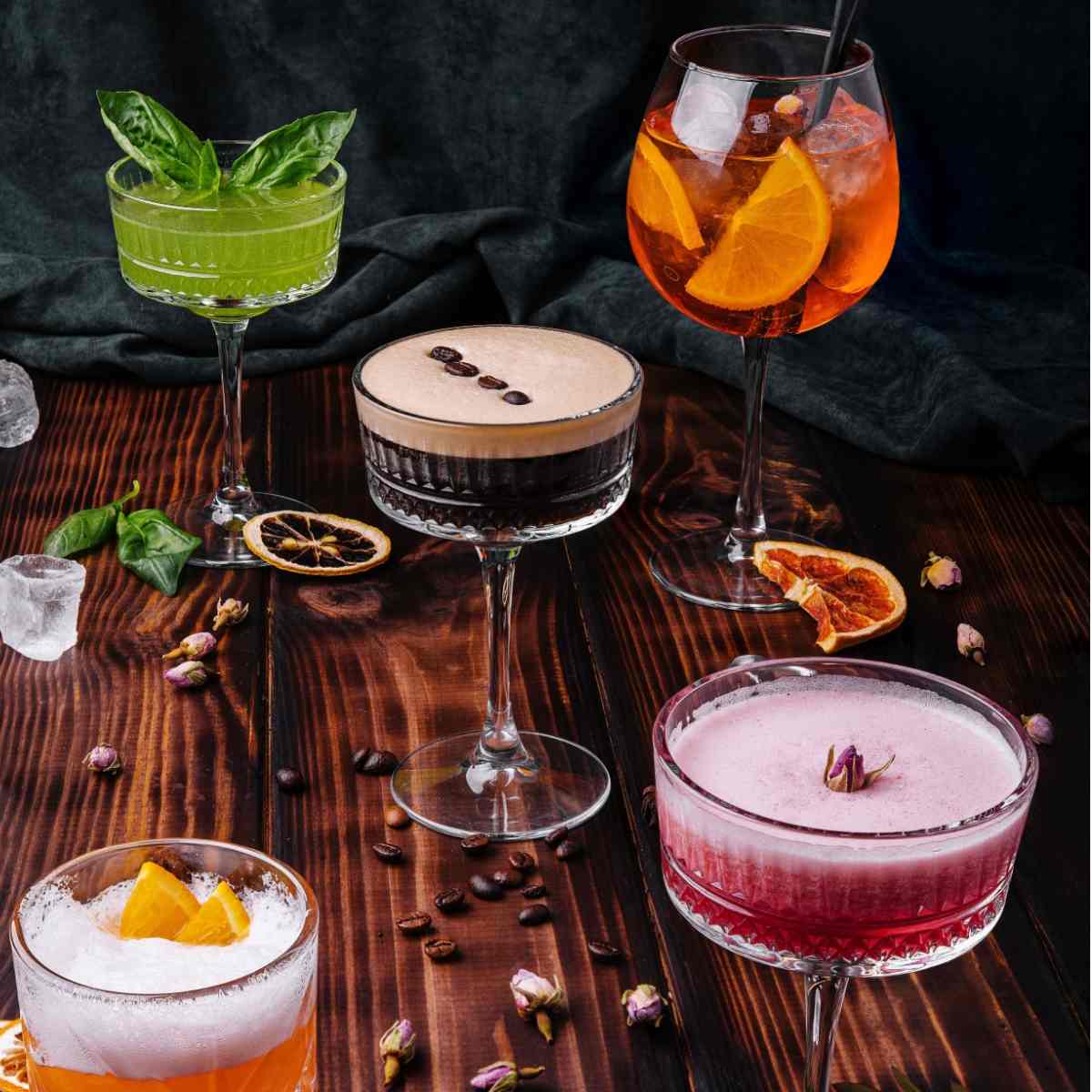Five great cocktails in various glassware on a wooden table.