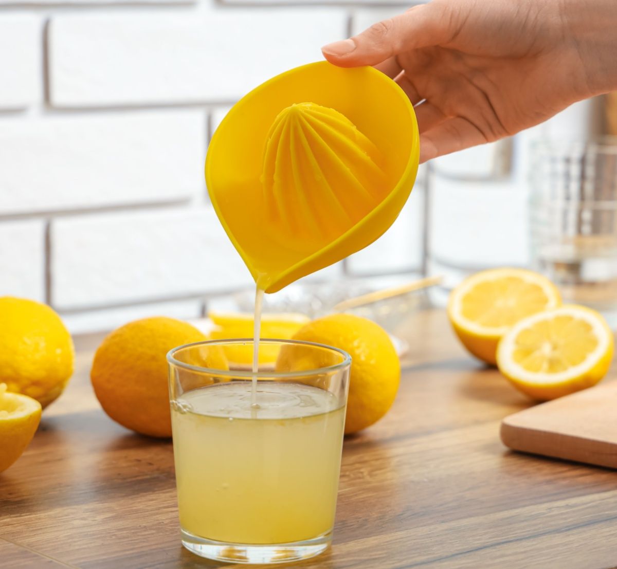 A person pouring lemon juice into a glass from a yellow juicer.