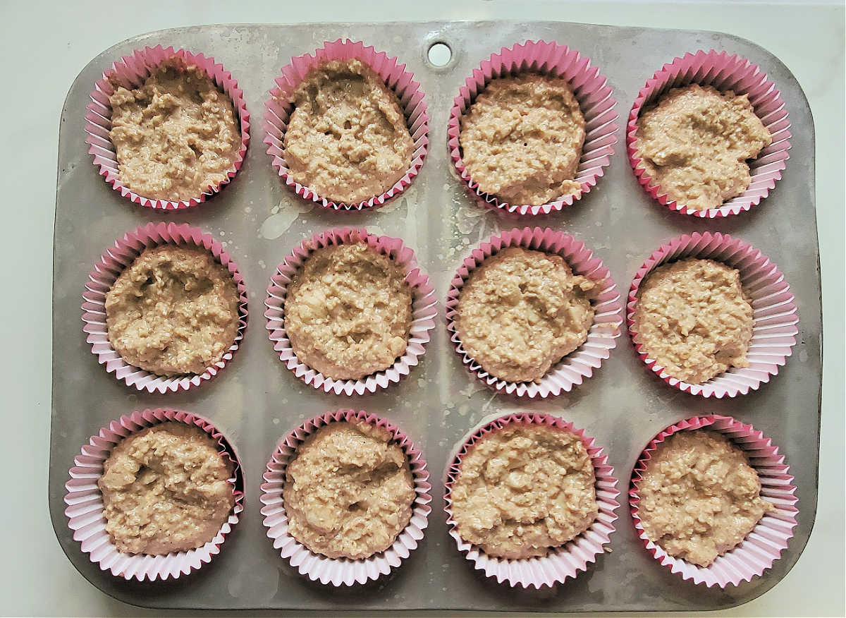 Apple muffin batter in paper liners in a muffin pan.