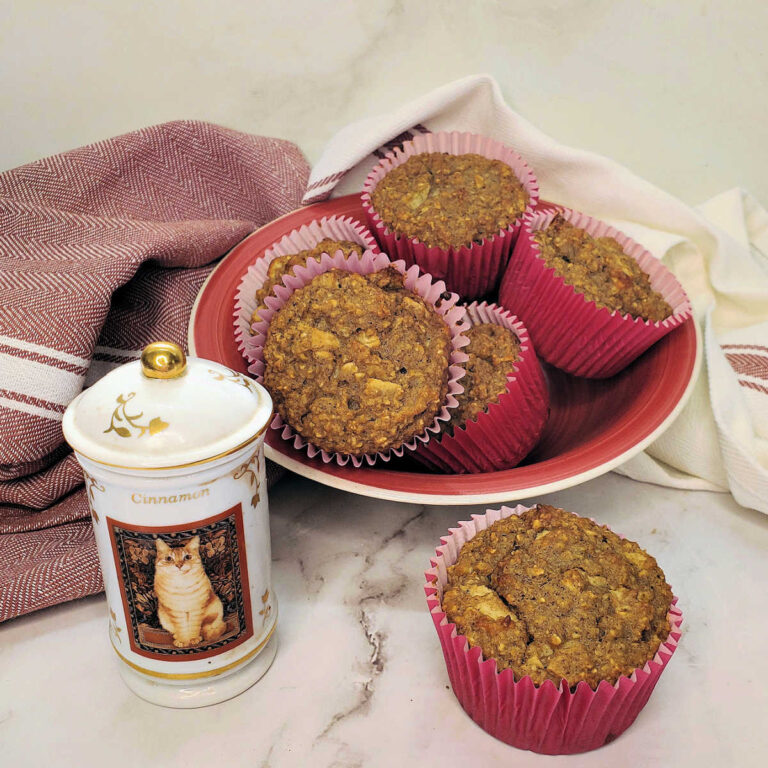 Apple oatmeal muffins with yogurt in a red bowl with a jar of cinnamon.