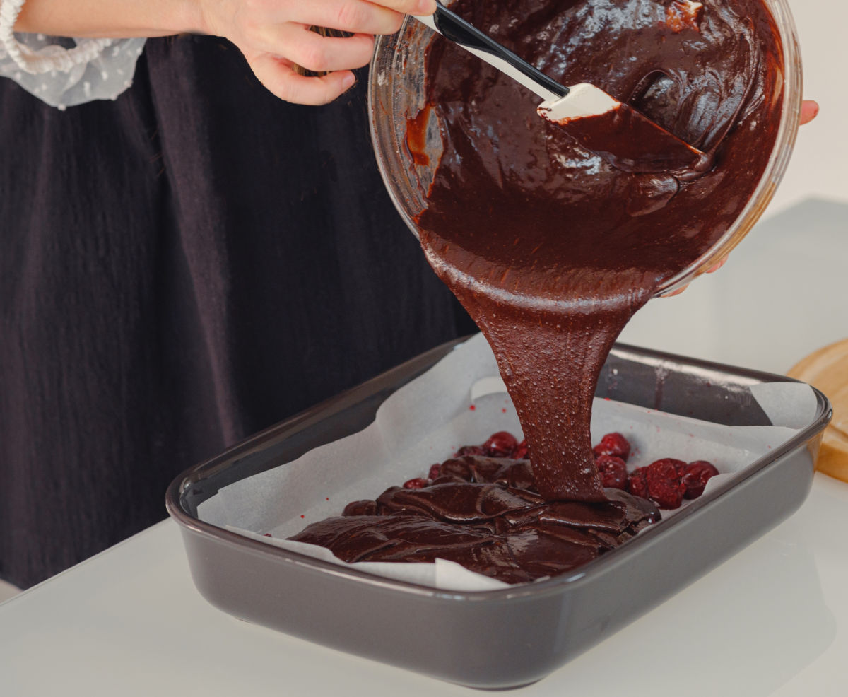A woman pouring baileys brownies batter into a baking pan lined with parchment paper.