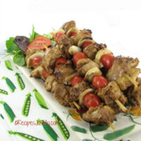 A chicken skewers Chinese recipe on a plate next to a green and white towel.