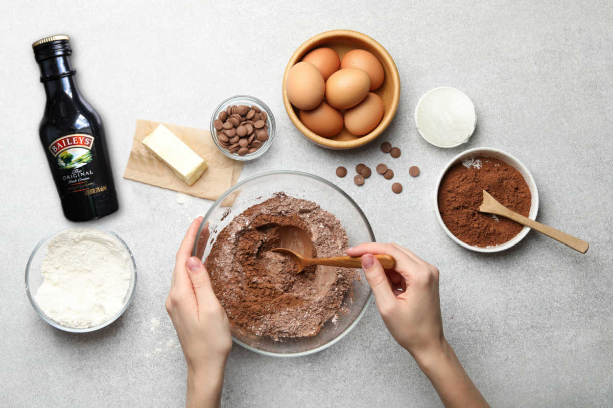 Baileys Irish cream, eggs, butter, cocoa, sugar, flour, chocolate chips on a counter top.
