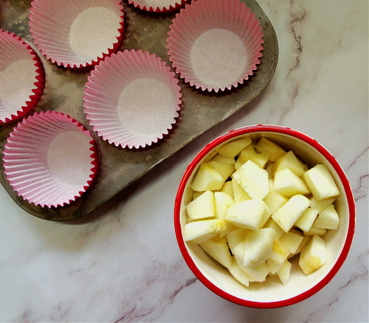 A muffin pan with paper liners next to a bowl of diced honey crips apples.