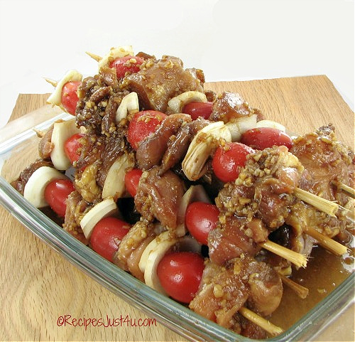 A pile of marinated chicken skewers with onions and tomatoes ready to grill.