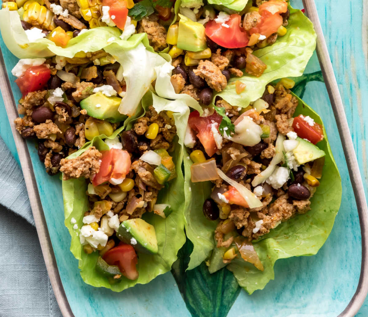 Mexican lettuce taco wraps on a blue plate topped with fresh veggies.