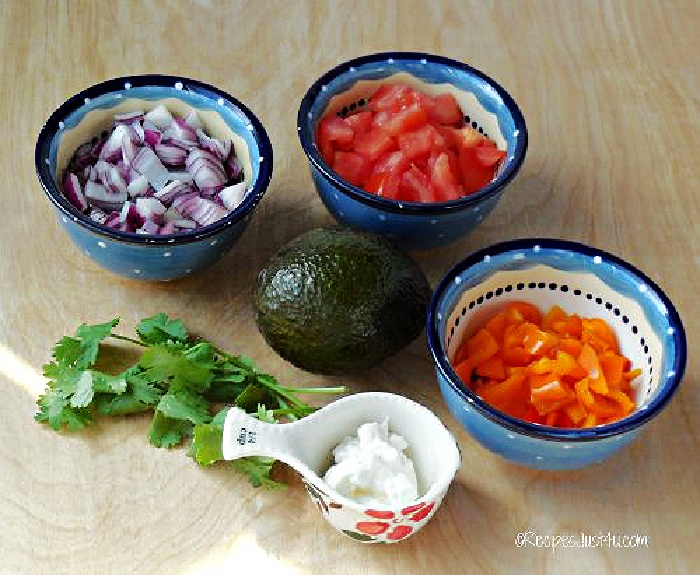 Toppings for lettuce wrap tacos in bowls, including onions, tomatoes, peppers, light sour cream and avocado.