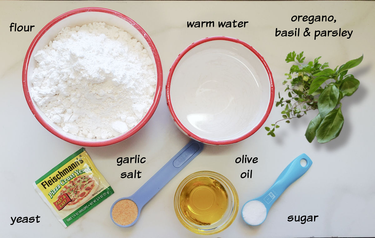Ingredients for the Italian herb bread recipe in bowls and spoons on a marble countertop.