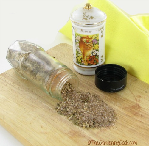 A jar of Caribbean jerk dry rub spilling out on a cutting board.