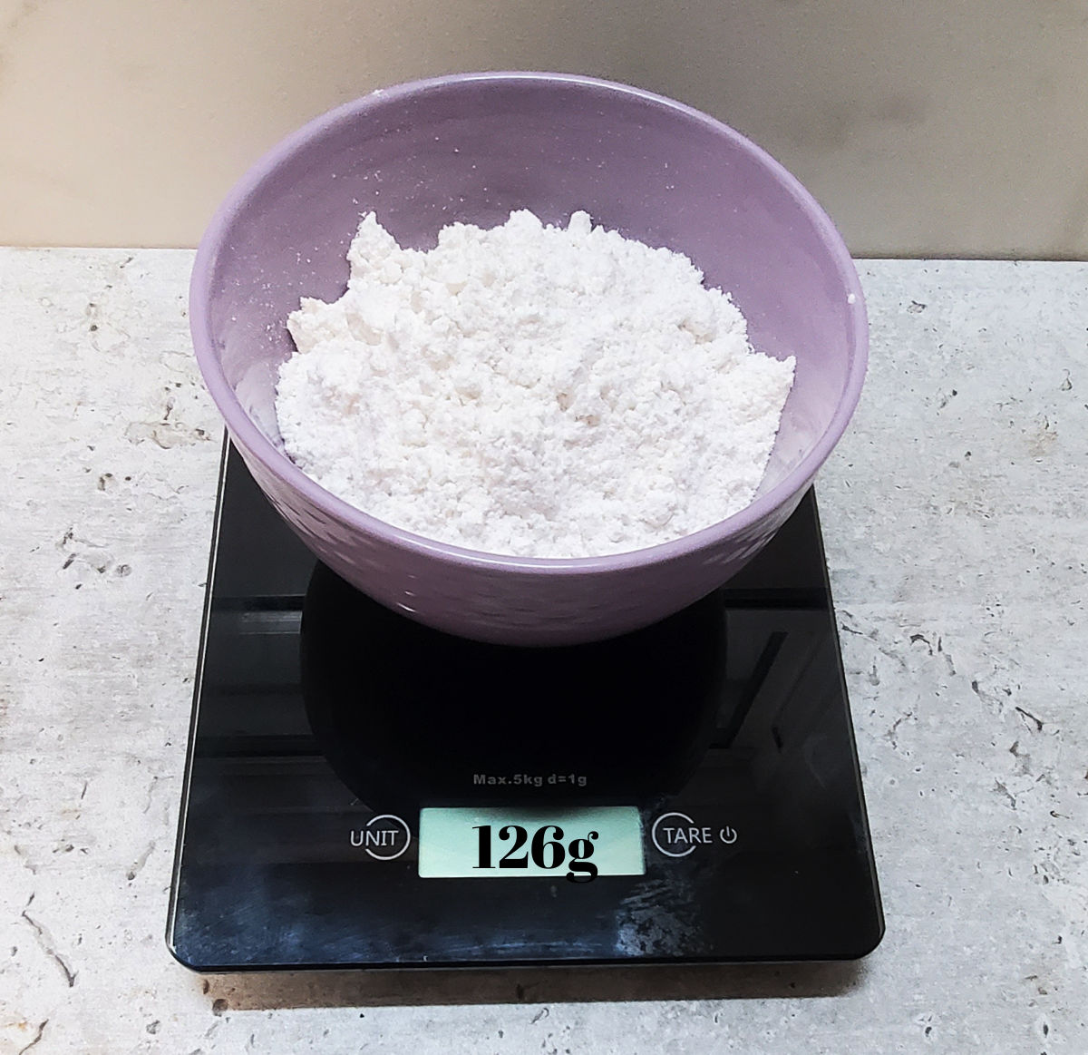 A purple bowl with flour in it on a digital scale weighing 126g.