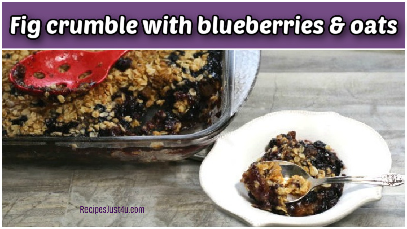 Fig crumble with blueberries and oats in a white bowl with a spoon next to a serving dish.
